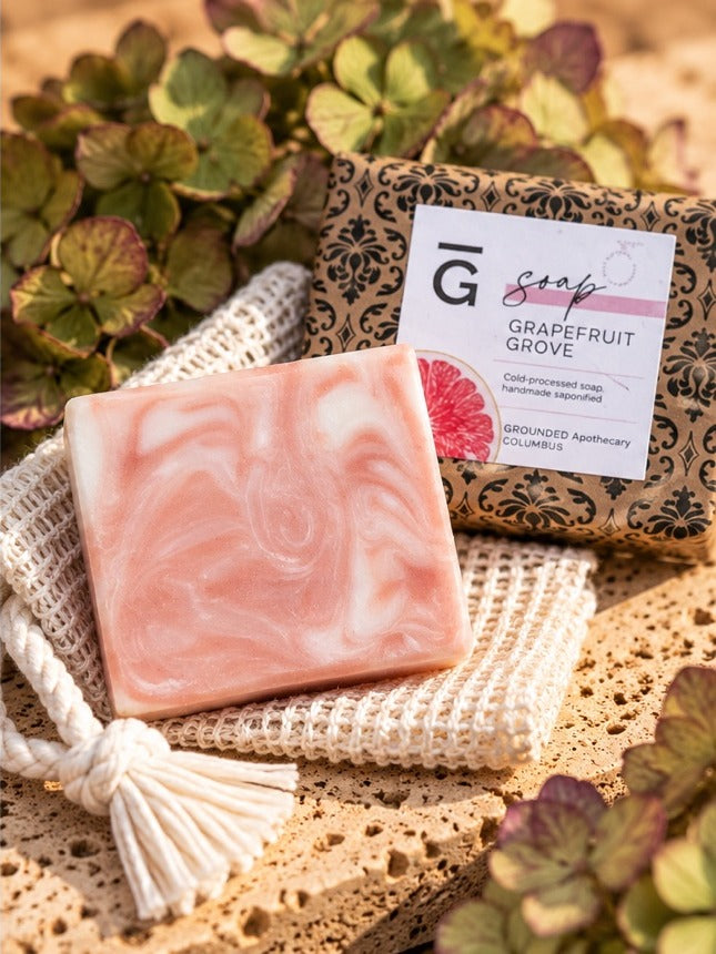 Grapefruit Grove tallow soap bar with kaolin clay and grapefruit, unwrapped bar beside its wrapped bar and a jute soap saver bag
